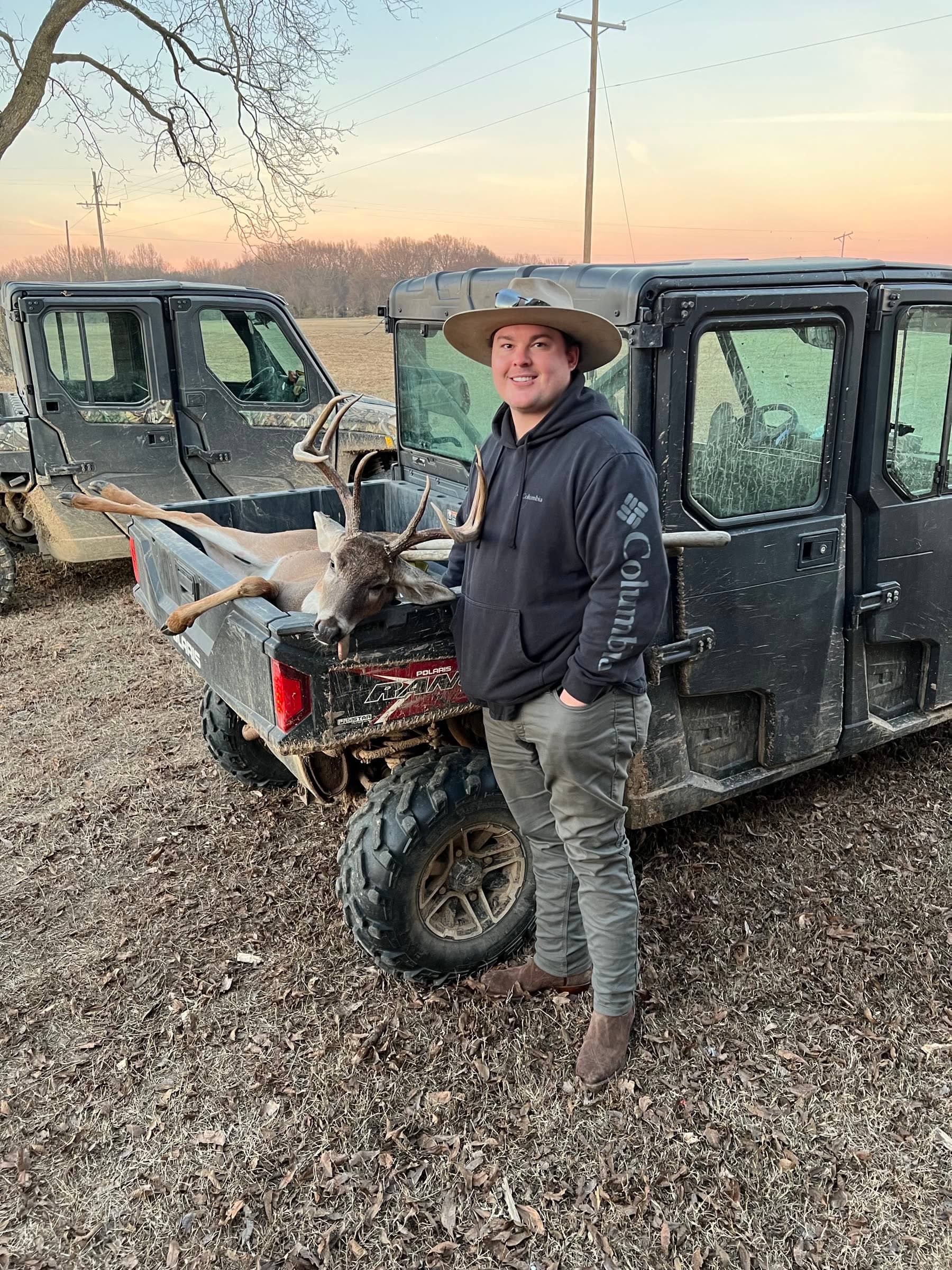 A family member beside a deer and utility vehicles after a hunt