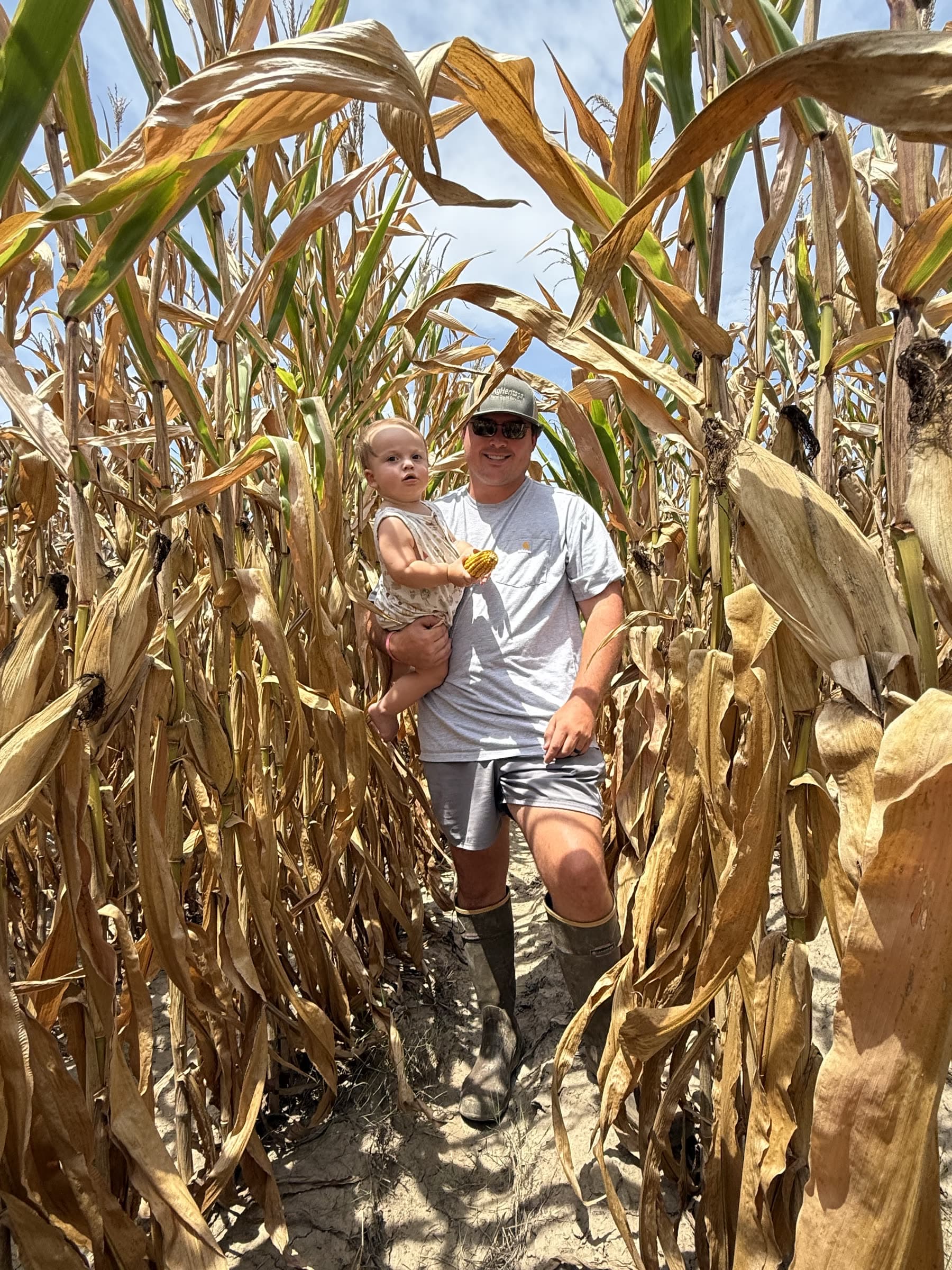 A Witham family member holding a young child in a cornfield