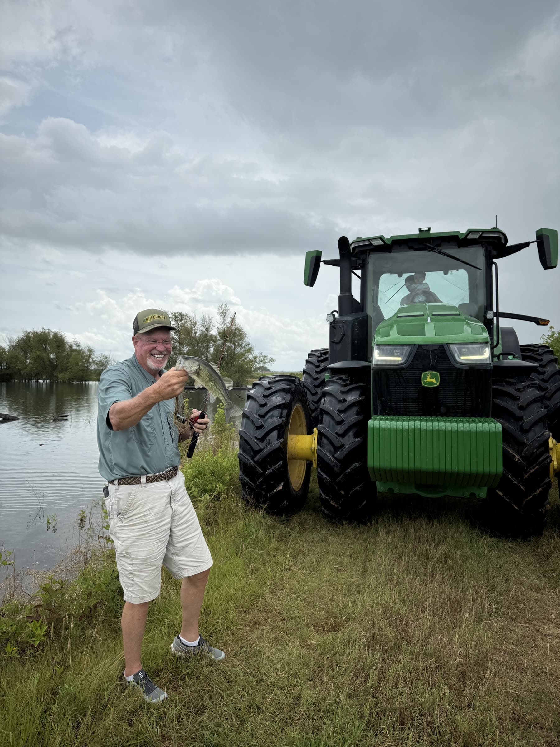 A family member holding a fish beside a tractor and pond