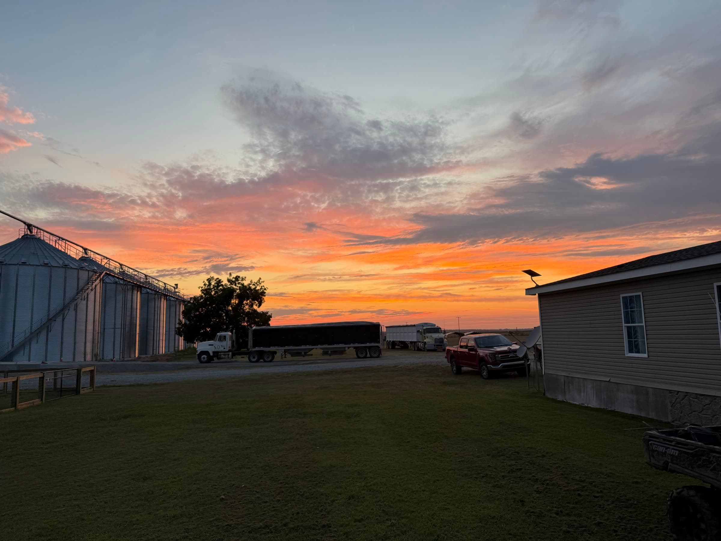 Grain bins and trucks beneath an orange Arkansas sunset