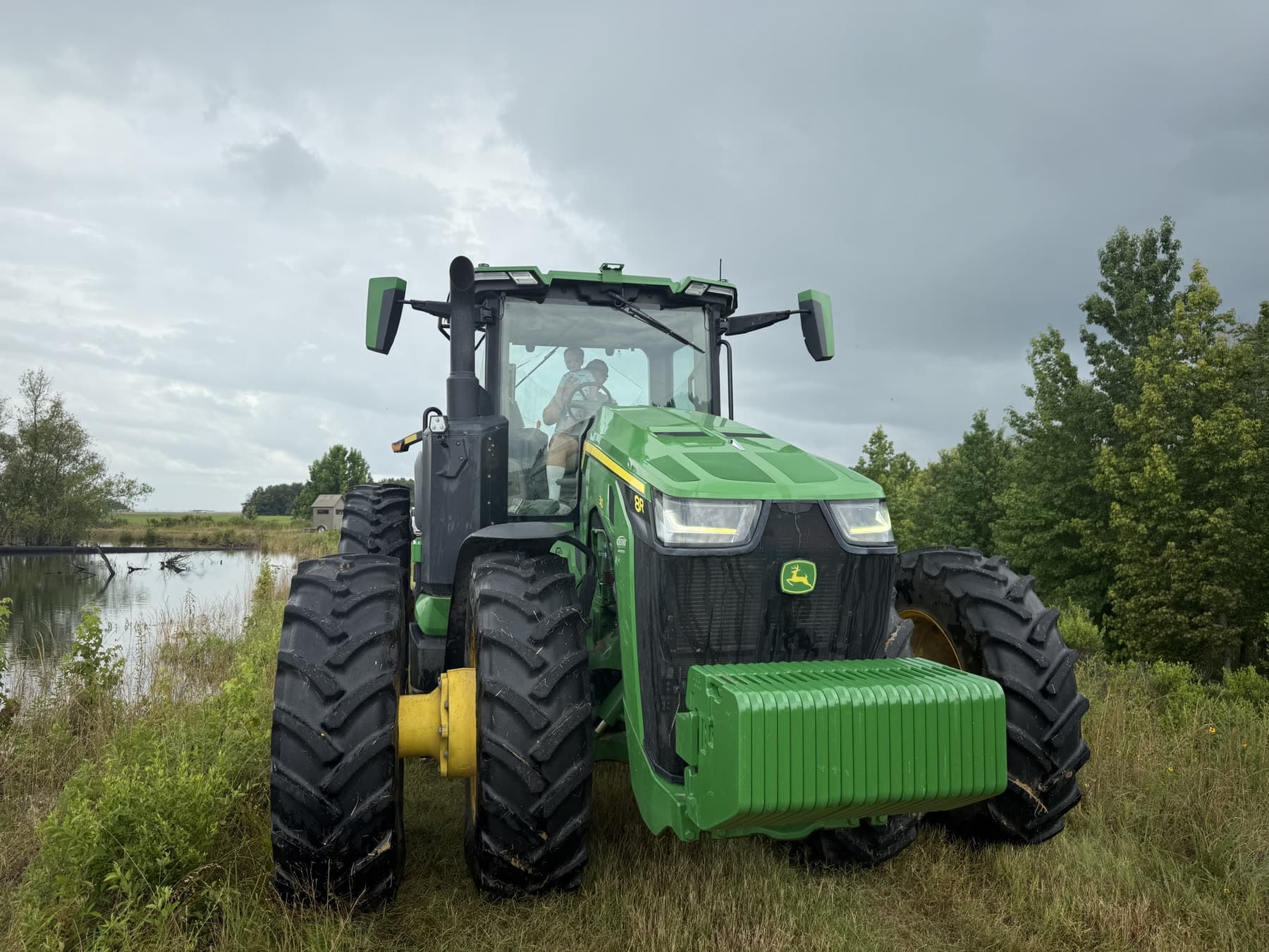 A green tractor parked beside a farm pond